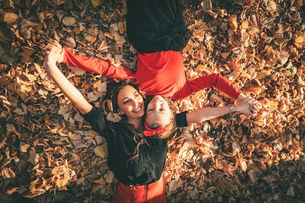 Belle jeune femme et sa petite fille profitent des couleurs de la forêt ensoleillée d'automne. Ils sont allongés sur des feuilles jaunes dorées et s'amusent.