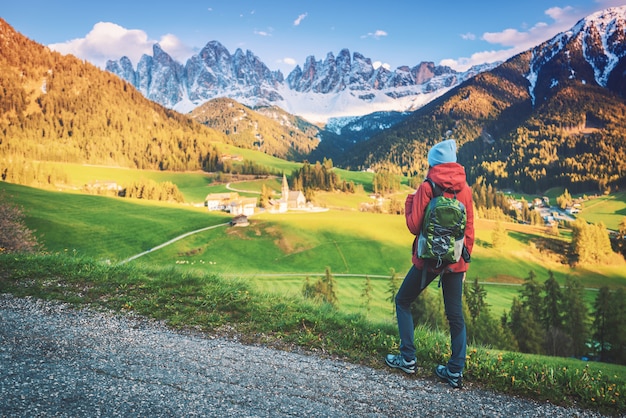 Belle jeune femme avec sac à dos est debout sur la colline dans les montagnes au coucher du soleil en automne.