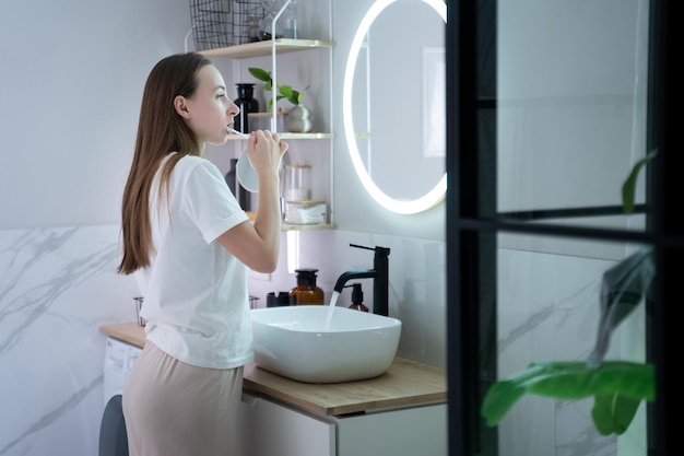 Belle jeune femme se brosse les dents debout devant le miroir de la salle de bain une femme heureuse tient un