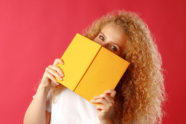 Belle jeune femme se cachant derrière le livre contre le rose