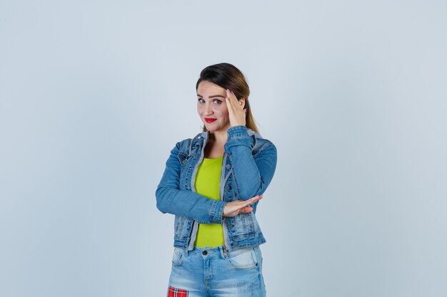 Belle jeune femme se cachant le visage derrière la main en tenue de denim et l'air honteux. vue de face.