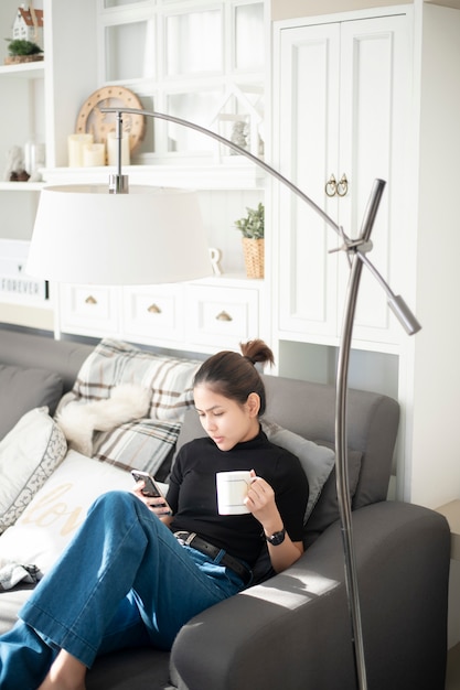 Belle jeune femme se détendre sur le canapé à la maison et à l&#39;aide de téléphone intelligent