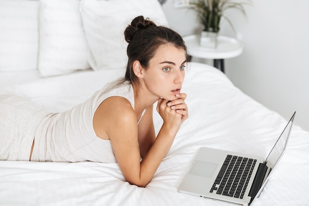 Belle jeune femme se détendre sur le lit à la maison, à l'aide d'un ordinateur portable