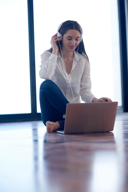 belle jeune femme se détendre et travailler sur un ordinateur portable bureau à domicile moderne tout en écoutant de la musique sur un casque blanc