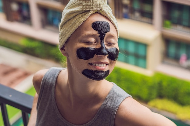 Belle jeune femme se relaxant avec un masque facial à la maison heureuse femme joyeuse appliquant un masque noir sur le visage