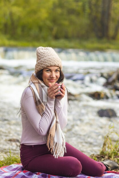 Une belle jeune femme se repose sur les rives d'une rivière d'automne