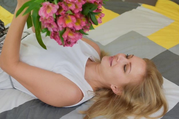 belle jeune femme se trouve sur le lit avec un bouquet de fleurs fraîches