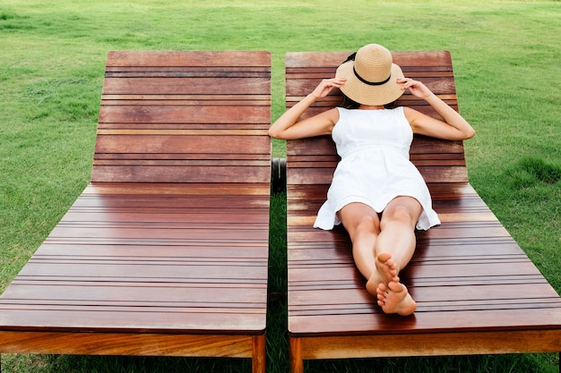 Belle jeune femme se trouve et repose sur une chaise longue en bois