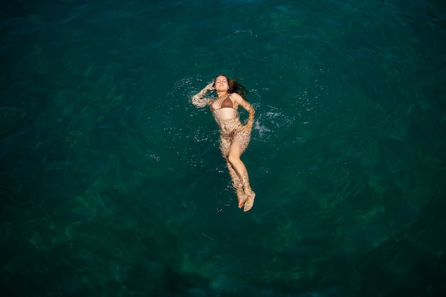 Une belle jeune femme séduisante en maillot de bain se trouve à la surface de l'eau à la mer. Vue d'en-haut. Elle profite de ses vacances. Mise au point sélective