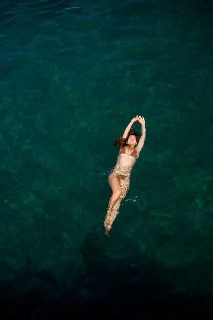 Une belle jeune femme séduisante en maillot de bain se trouve à la surface de l'eau à la mer. Vue d'en-haut. Elle profite de ses vacances. Mise au point sélective
