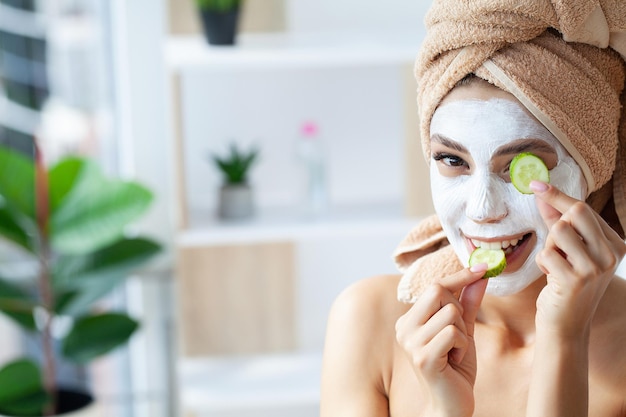 Belle jeune femme avec une serviette enroulée autour de sa tête en appliquant un masque facial à la salle de bain