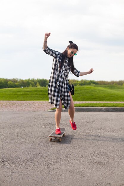 Belle jeune femme en slip patine sur l'asphalte en chaussures roses sur le fond