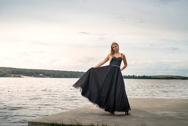 Belle jeune femme en soirée longue robe noire près de l'étang, mode de vie estival