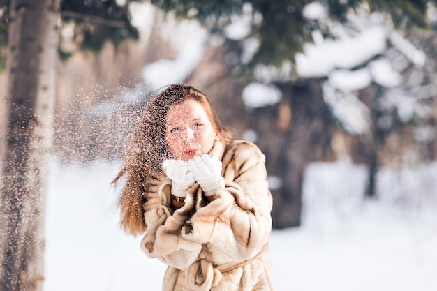Belle jeune femme soufflant de la neige en hiver