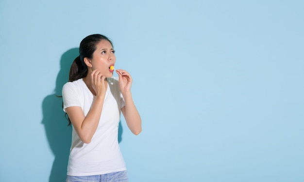 belle jeune femme souffrant de maladie des dents sensibles debout sur fond de mur bleu mangeant des bonbons à la sucette en regardant la zone vide s'inquiéter de la carie dentaire.