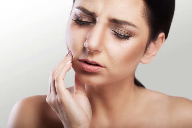 Belle jeune femme souffrant de maux de dents, caries, problèmes dentaires, sensations douloureuses sur son visage, beau maquillage.