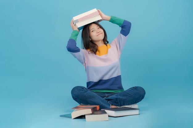 Une belle jeune femme soulève de nombreux livres sur la tête tout en souriant joyeusement