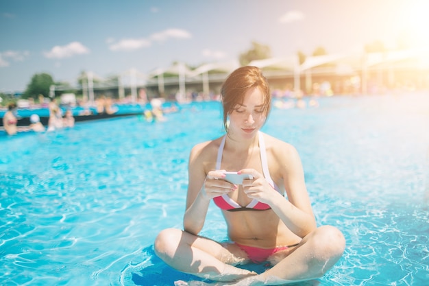 Belle jeune femme souriante en bikini dans la piscine chaude de la station et parler au téléphone mobile.