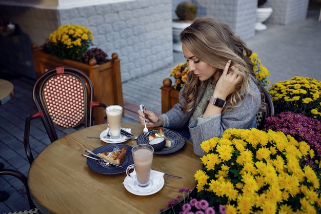 Belle jeune femme souriante et boire du café dans le café en plein air de la rue