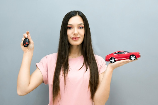 Belle jeune femme souriante avec des clés de voiture et une voiture à la main Le concept d'apprentissage dans une auto-école et l'achat d'une nouvelle voiture sur fond gris