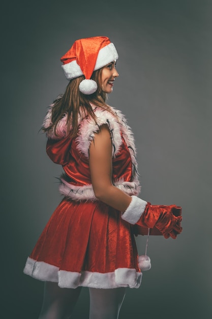 Belle jeune femme souriante en costume de père Noël tenant un cadeau rouge.