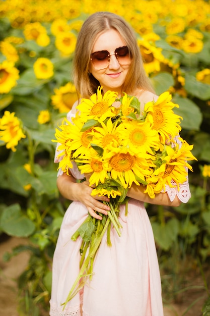 Belle jeune femme souriante dans une chemise blanche se dresse dans le champ parmi les tournesols