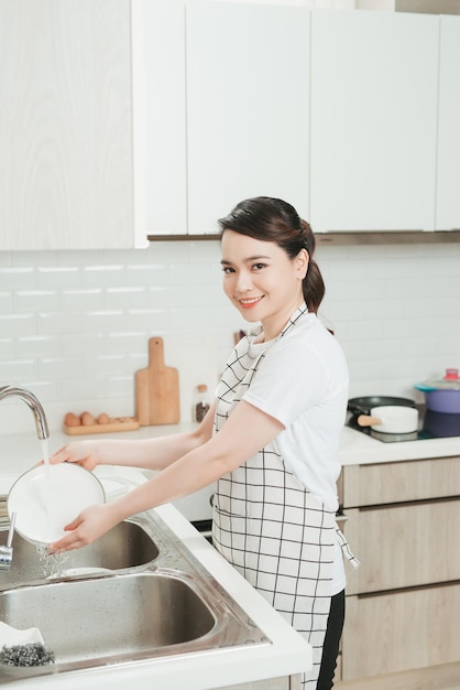 Belle jeune femme souriante faisant la vaisselle dans une cuisine blanche moderne