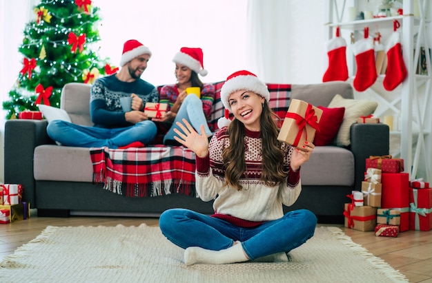 Belle jeune femme souriante heureuse dans un pull de Noël et bonnet de Noel tient une boîte-cadeau