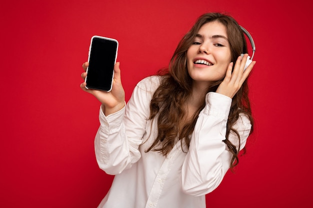 Belle jeune femme souriante et heureuse portant une tenue décontractée élégante isolée sur le mur de fond