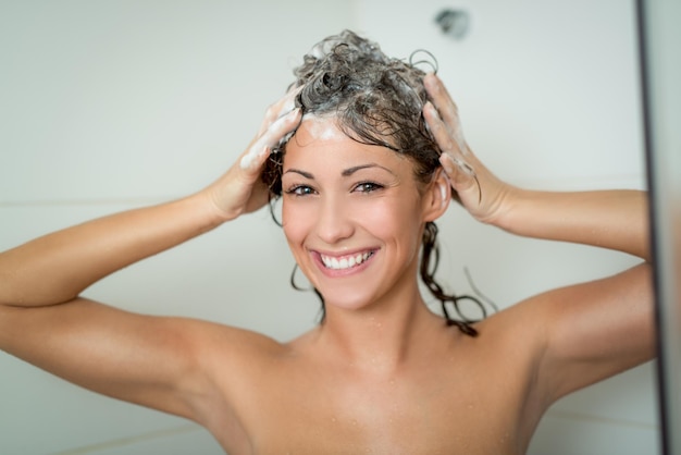 Belle jeune femme souriante lavant ses longs cheveux avec du shampoing.