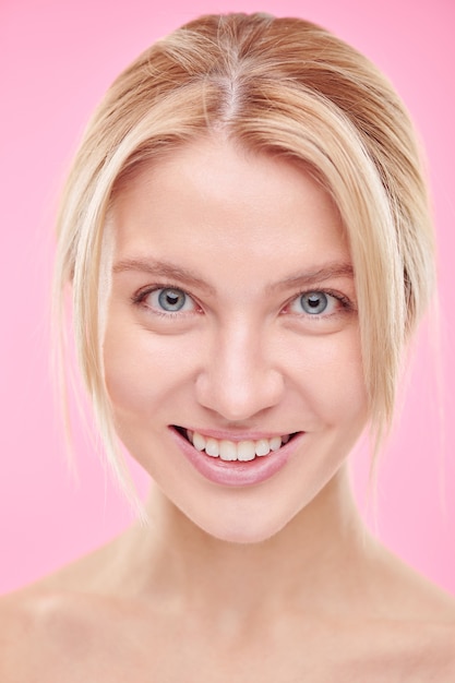 Photo belle jeune femme souriante avec un maquillage naturel isolé contre le mur rose