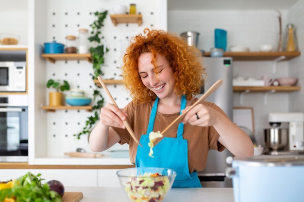 Belle jeune femme souriante mignonne dans la cuisine prépare une salade végétalienne dans des vêtements décontractés