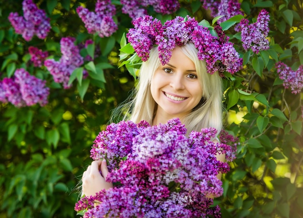 Belle jeune femme souriante porte une couronne et un bouquet de fleurs lilas