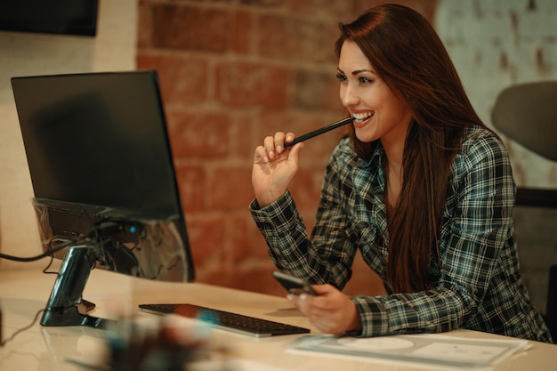 Belle jeune femme souriante réussie analyse un nouveau projet sur son ordinateur au bureau.