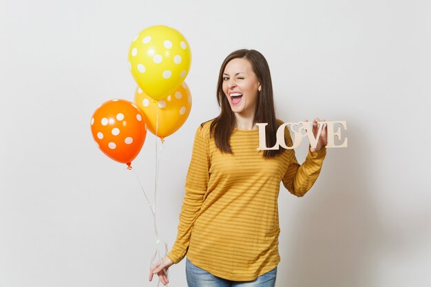 Belle jeune femme souriante romantique tenant le mot amour en bois, ballons à air orange jaune sur fond blanc. Copiez l'espace pour la publicité. Concept de la Saint-Valentin ou de la Journée internationale de la femme.
