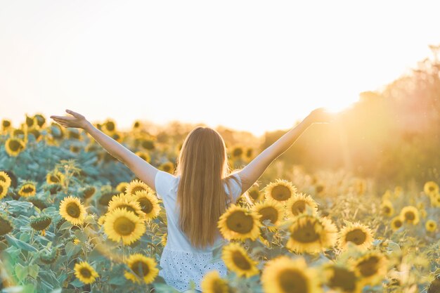 Belle jeune femme souriante et s'amuser dans un champ de tournesol par une belle journée d'été.