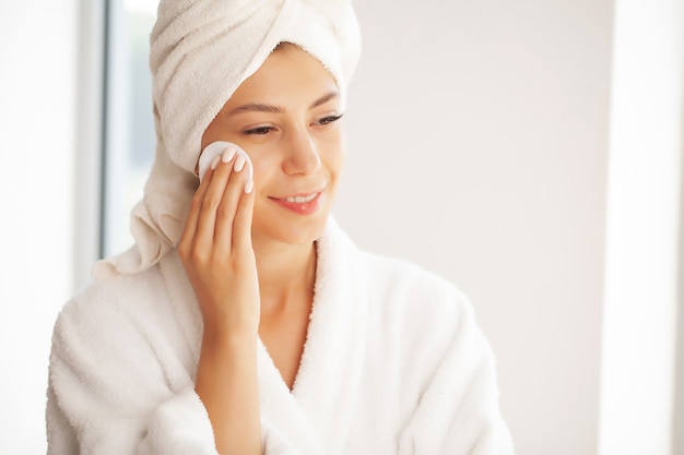 Belle jeune femme souriante se maquiller avec une lingette faciale.