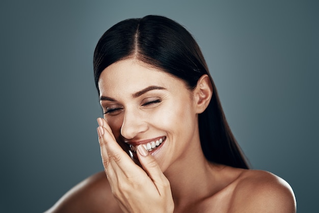 Belle jeune femme et souriante en se tenant debout contre le mur gris