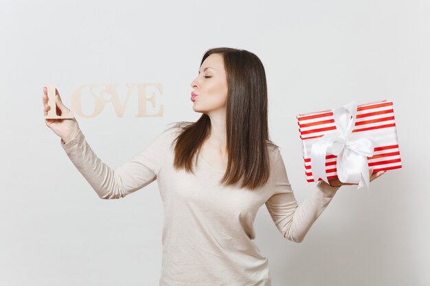 Belle jeune femme souriante sexy tenant une boîte cadeau rouge avec cadeau, amour de mot en bois sur fond blanc. Copiez l'espace pour la publicité. Concept de la Saint-Valentin ou de la Journée internationale de la femme.