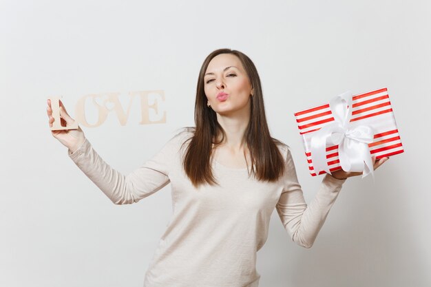 Belle jeune femme souriante sexy tenant une boîte cadeau rouge avec cadeau, amour de mot en bois sur fond blanc. Copiez l'espace pour la publicité. Concept de la Saint-Valentin ou de la Journée internationale de la femme.