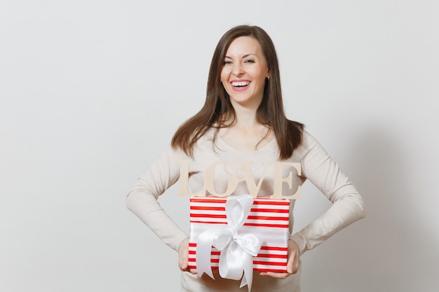 Belle jeune femme souriante sexy tenant une boîte cadeau rouge avec cadeau, amour de mot en bois sur fond blanc. Copiez l'espace pour la publicité. Concept de la Saint-Valentin ou de la Journée internationale de la femme.