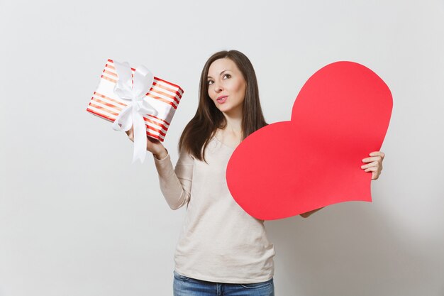 Belle jeune femme souriante tenant un grand coeur rouge, boîte avec cadeau sur fond blanc. Copiez l'espace pour la publicité. Avec place pour le texte. Concept de la Saint-Valentin ou de la Journée internationale de la femme.