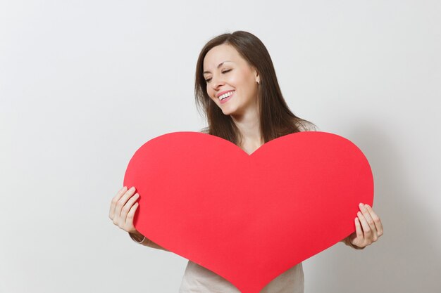 Belle jeune femme souriante tenant un grand coeur rouge dans les mains isolés sur fond blanc. Copiez l'espace pour la publicité. Avec place pour le texte. Concept de la Saint-Valentin ou de la Journée internationale de la femme.