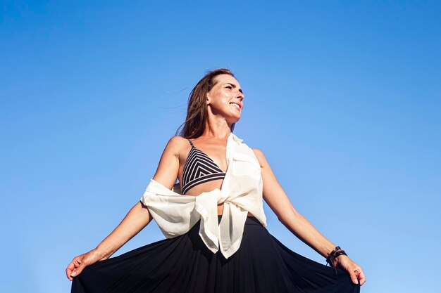 Belle jeune femme souriante tenant une jupe en se tenant debout sur une falaise.