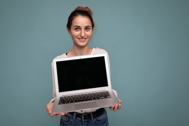 Belle jeune femme souriante tenant un ordinateur netbook regardant la caméra portant une chemise blanche