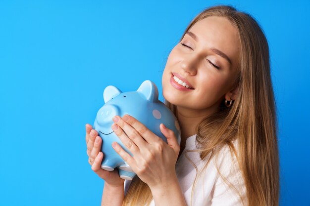 Belle jeune femme souriante avec tirelire sur fond bleu