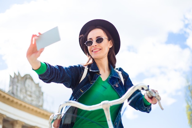 Belle jeune femme souriante sur un vélo faisant selfie au téléphone et souriant