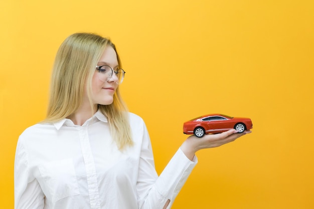 Belle jeune femme souriante avec une voiture à la main Le concept d'apprentissage dans une auto-école et l'achat d'une nouvelle voiture sur fond jaune