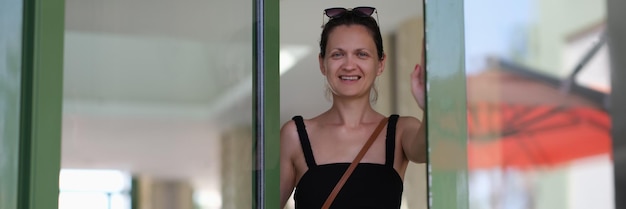 La belle jeune femme de sourire ouvre la porte en verre