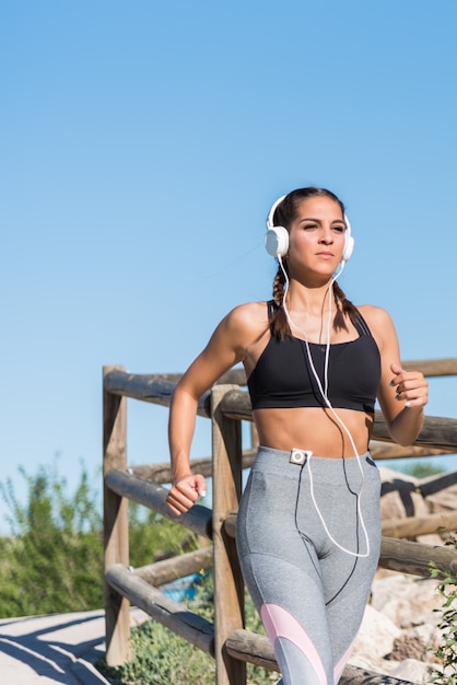 Belle jeune femme sportive courir le jogging dans un parc à l'extérieur écouter de la musique